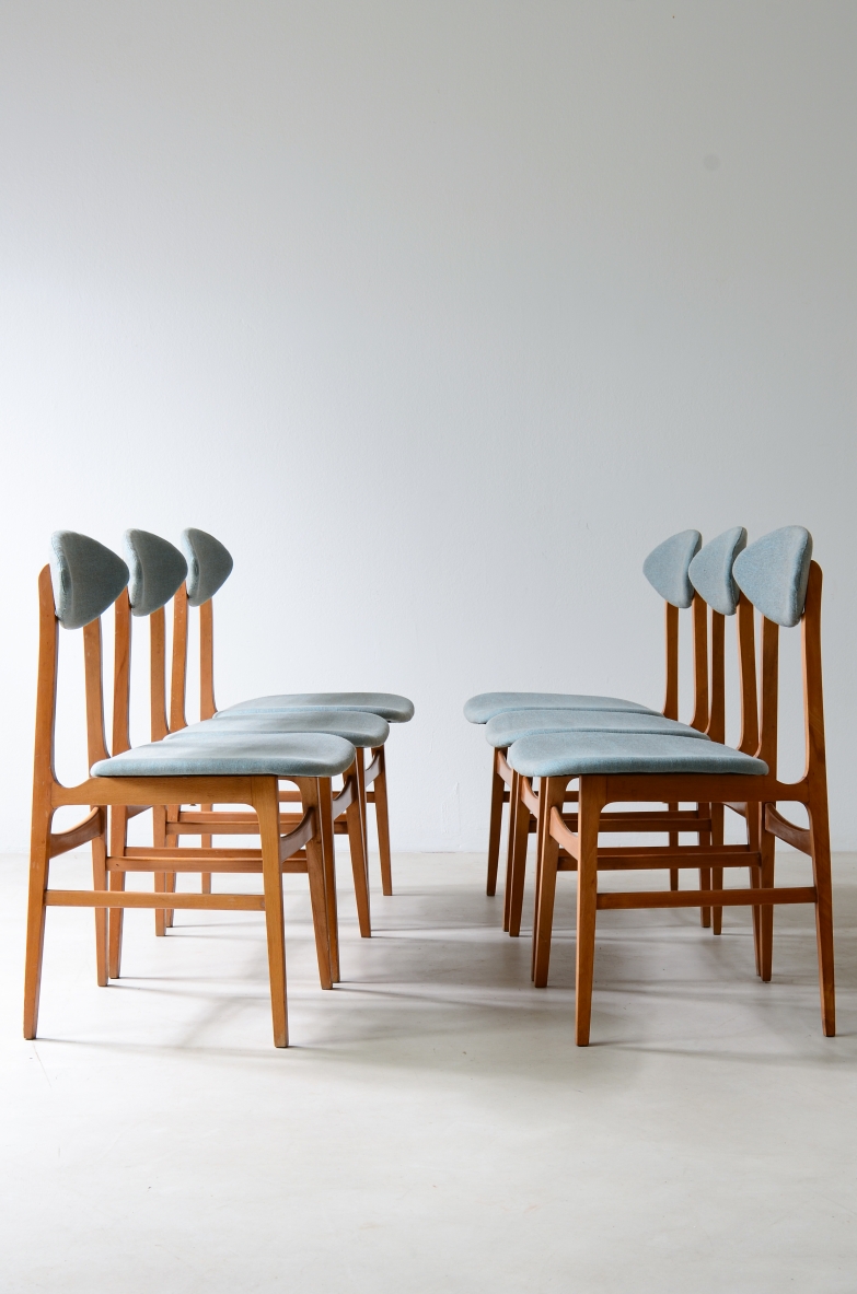 Group view of six 1960s Italian chairs arranged in two facing rows, with light wooden frames, pointed upholstered backrests and light blue fabric seats.