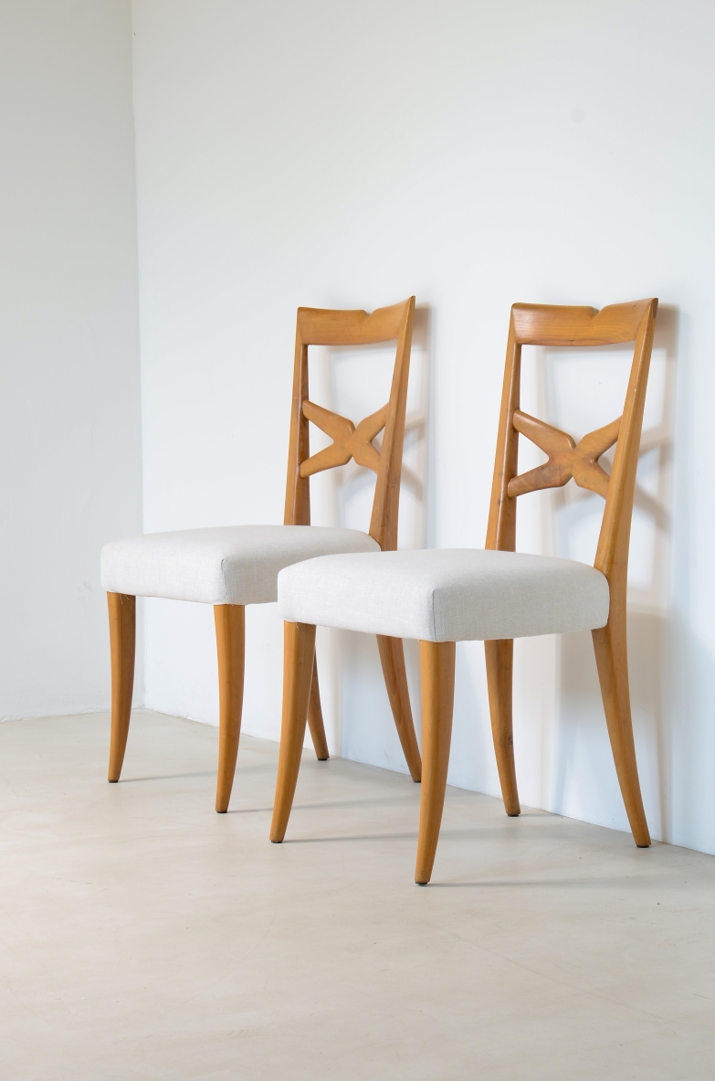Angled view of two Enrico Ciuti chairs in light walnut, with open X-shaped backrests, white upholstered seats and tapered wooden legs.