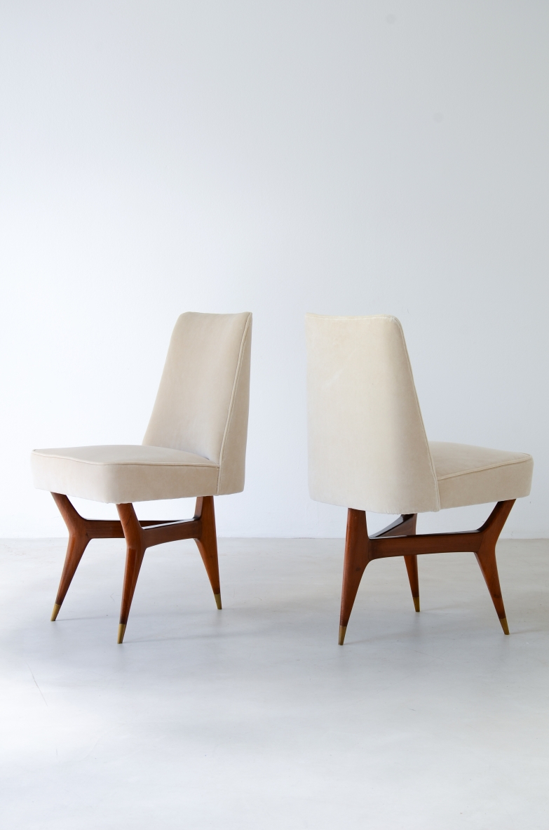 Two Melchiorre Bega chairs with white upholstered seats and tall backrests, wooden frames and tapered legs with brass feet, shown from the side and rear.