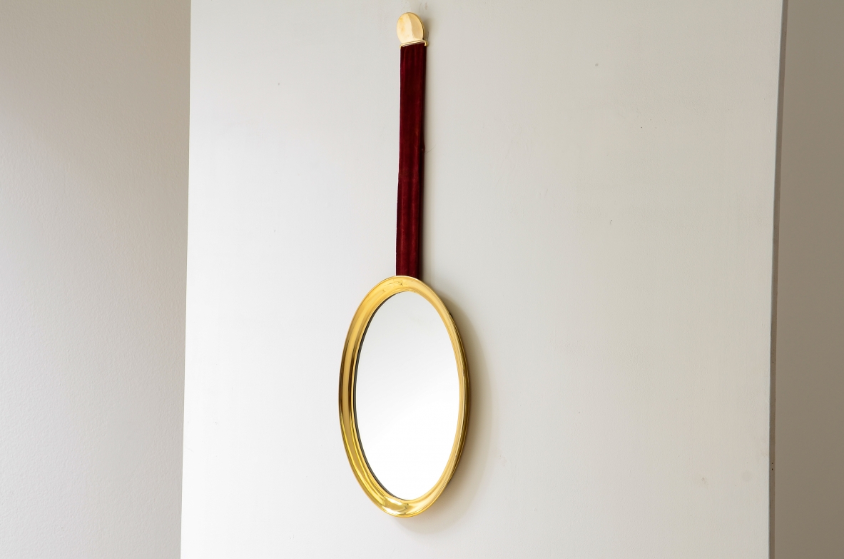 Specchiera in ottone sagomato appesa a un nastro in velluto originale e fissata a parete mediante un disco in ottone.  Manifattura italiana anni 50/60ca.