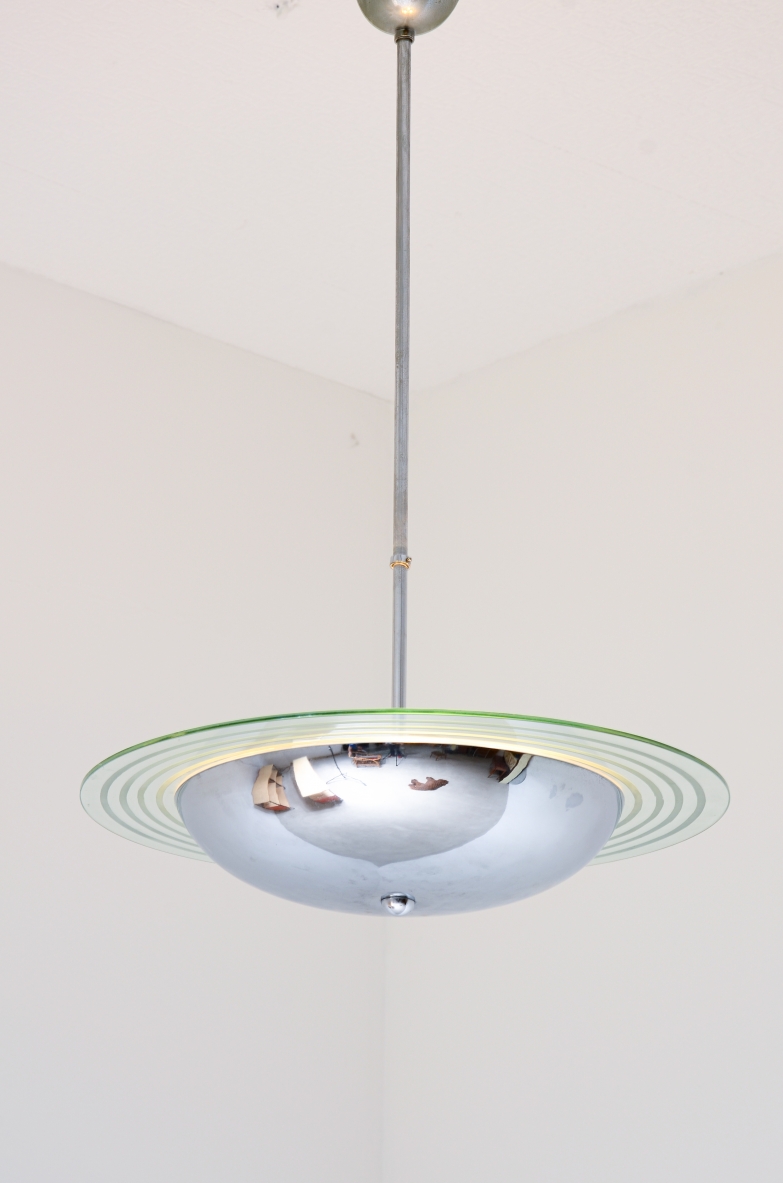 Italian chandelier, featuring a chrome-plated metal structure, central hemispherical diffuser and large circular bevelled and engraved glass disc with concentric patterns, suspended from a long metal rod.