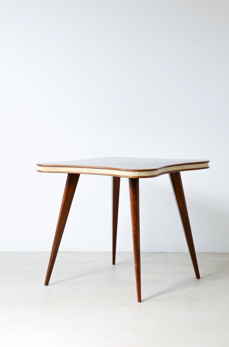 Italian table circa 1950 with quatrefoil-shaped walnut veneer top, parchment edging and four tapered legs, photographed in three-quarter view.