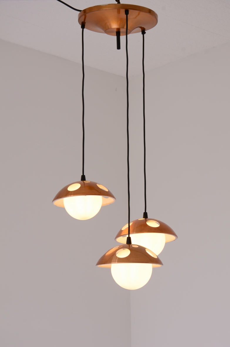 Italian three-light chandelier, featuring perforated copper mushroom-shaped shades and illuminated white opaline glass globes, suspended at varying heights by black cords from a circular copper ceiling canopy.