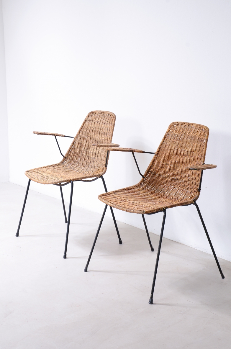 Angled view of two Franco Legler Basket armchairs with woven cane seats and backrests, armrests and slender black metal legs.