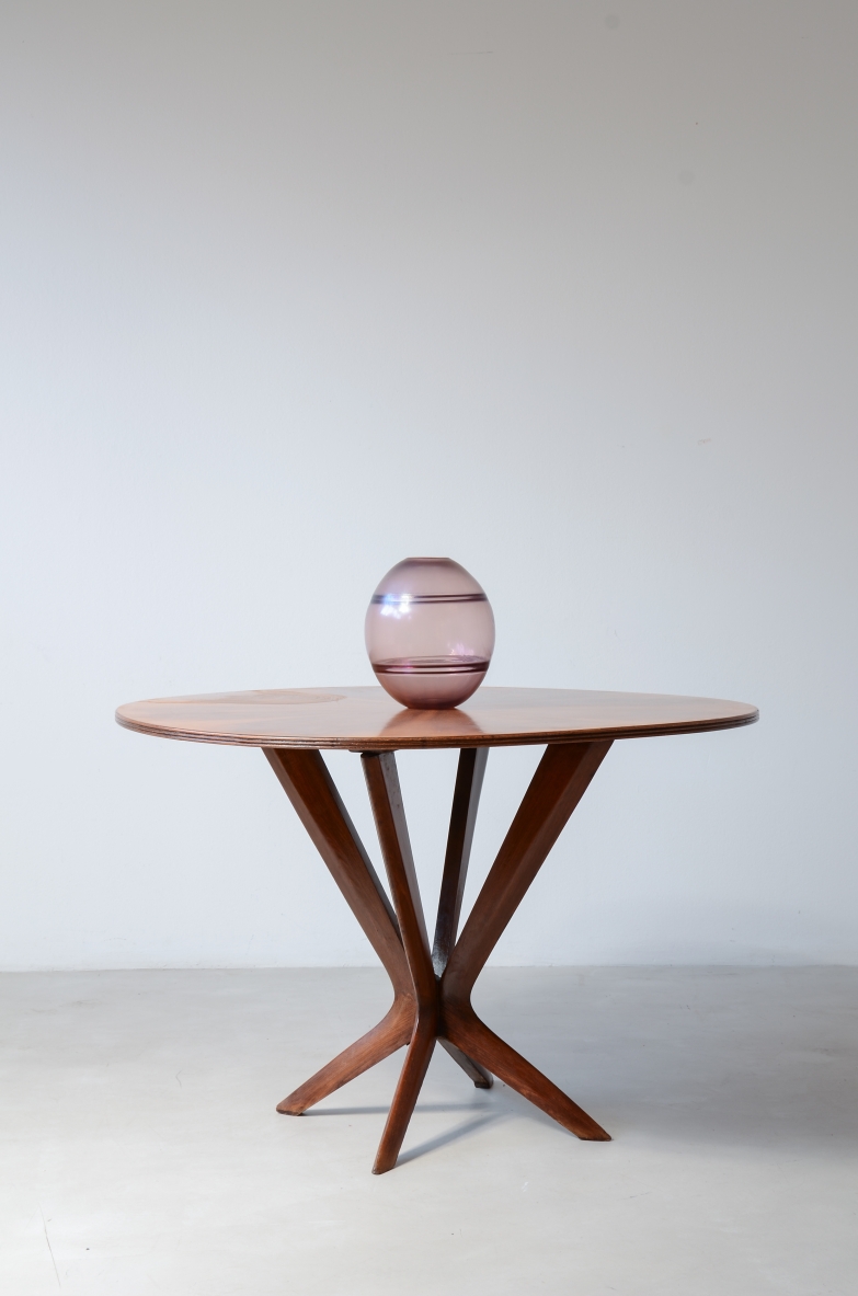 Italian 1950s table with an oval figured walnut top featuring a four-part veneer pattern, supported by a sculptural wooden pedestal with angled supports and splayed feet.