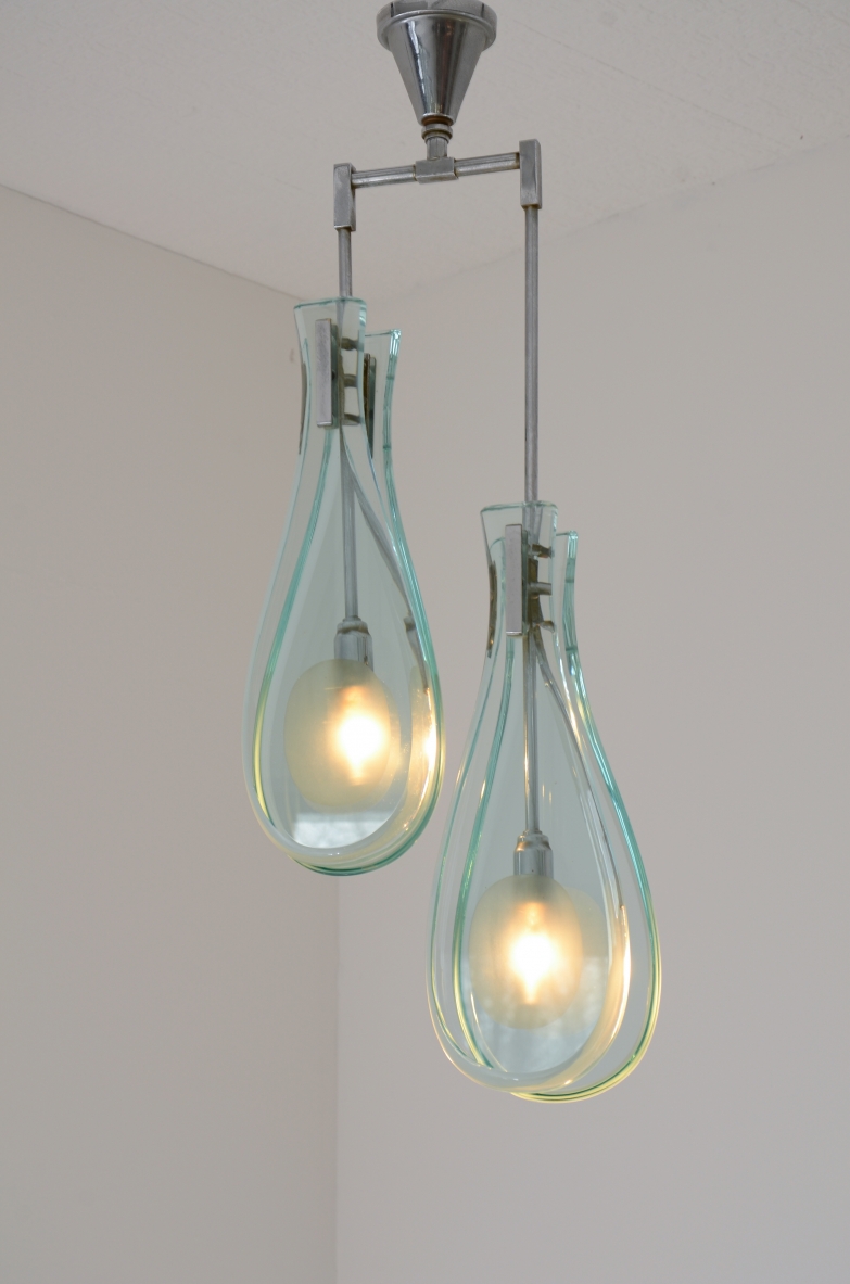 Max Ingrand model 2259/2 two-light chandelier for Fontana Arte, featuring thick transparent shaped glass teardrop diffusers suspended at different heights from a geometric metal frame, illuminated front view.