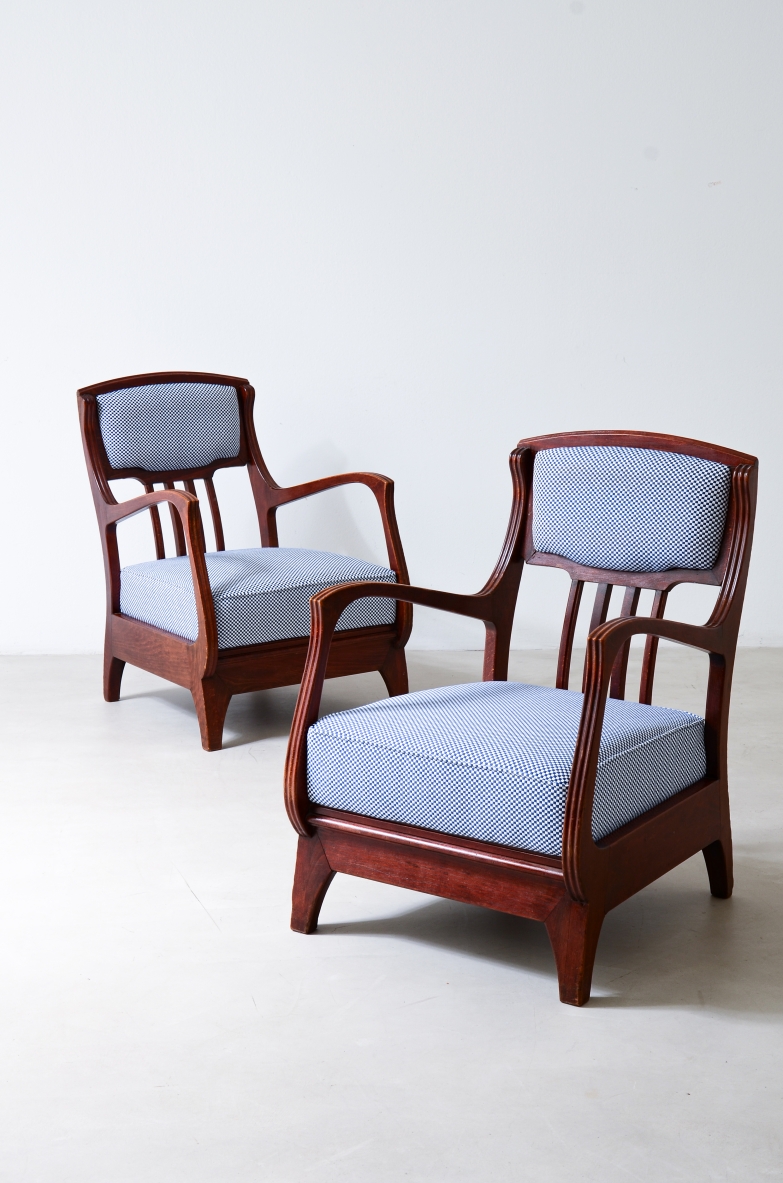 Coppia di poltrone Art Nouveau di Eugenio Quarti, con struttura in legno scuro sagomato, braccioli curvilinei, schienali con listelli verticali e sedute e schienali imbottiti in tessuto azzurro.