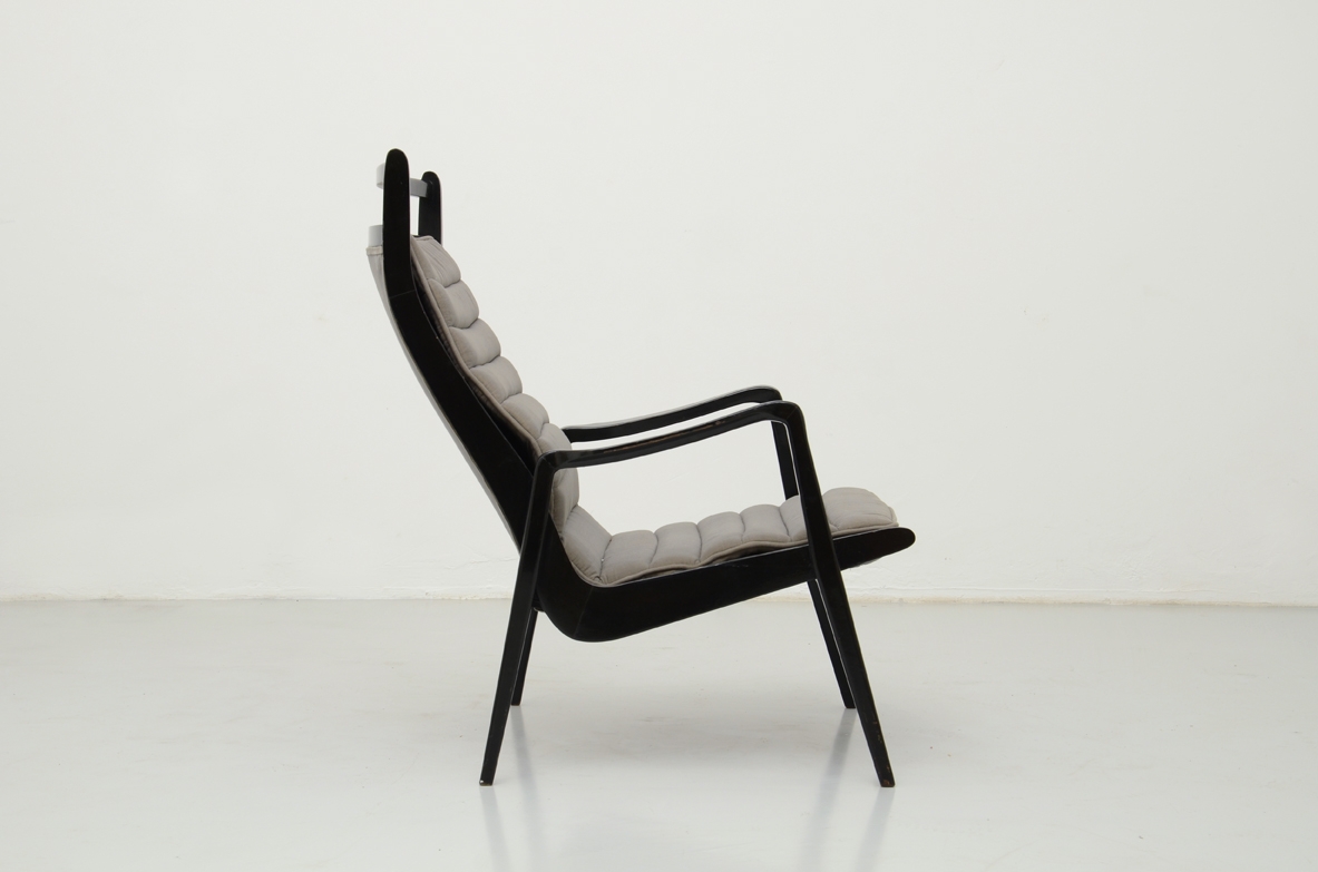 Italian 1950s reading armchair in the style of Gio Ponti, featuring an ebonized wooden frame, tall inclined backrest, grey channel-stitched upholstery, angular armrests and slender legs.