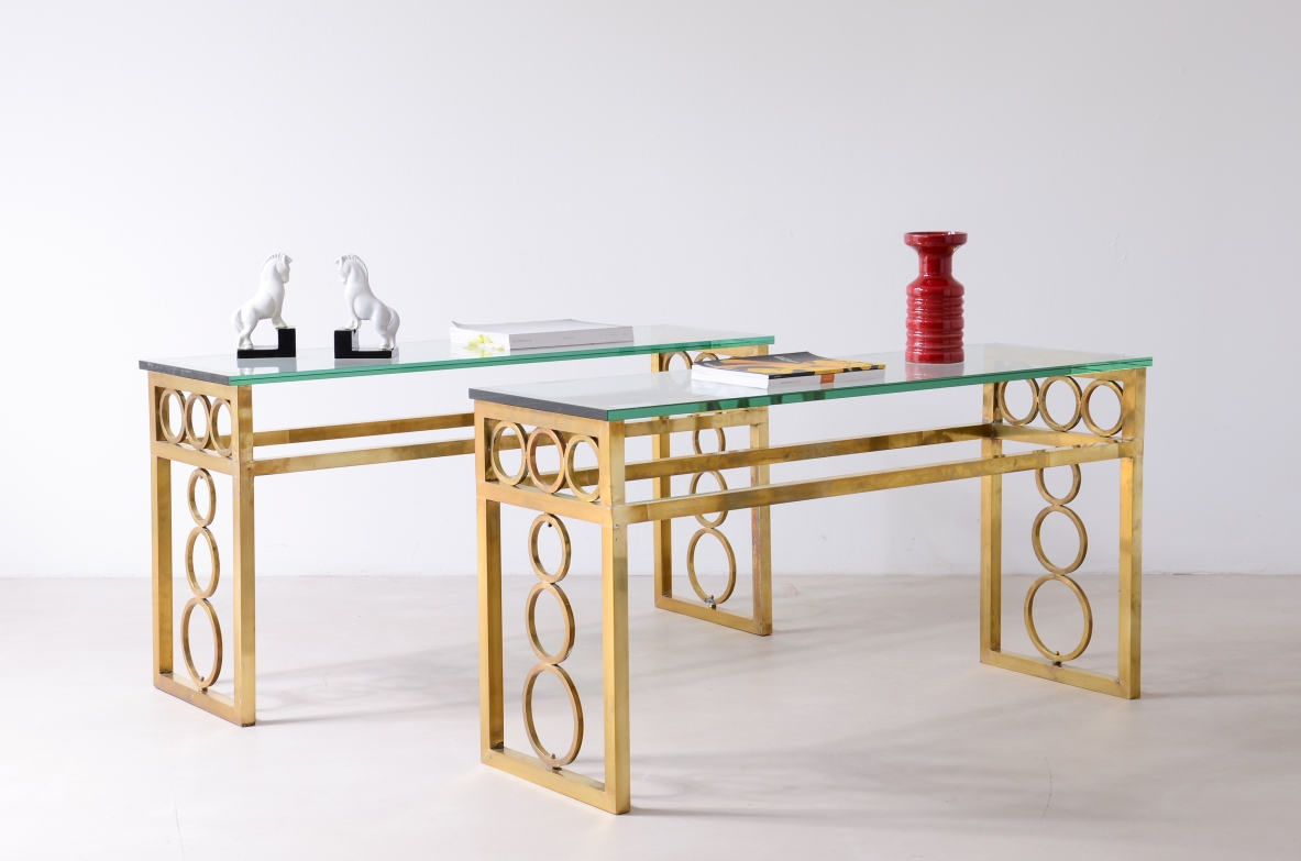 Pair of French console with brass frames, decorative side supports featuring interlocking circular geometric motifs and thick rectangular bevelled glass tops.