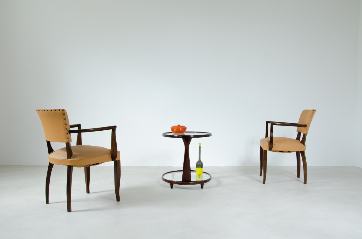 Group view of two French Art Deco armchairs positioned on either side of a small table, with dark wooden frames, geometric armrests and ochre-colored upholstery.