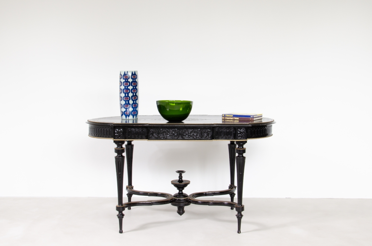 French ebonized wood center table, 1870–1900, with shaped oval top, brass detailing, four turned legs and curved stretchers with central decorative finial, front view.