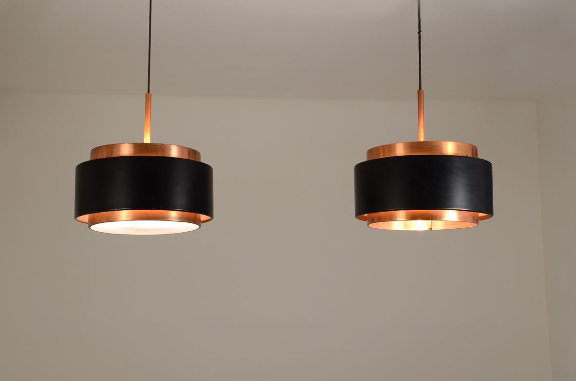 Pair of Saturn pendant lamps by Jo Hammerborg for Fog & Mørup,featuring cylindrical black lacquered metal shades, polished copper upper and lower bands and long suspension cords.