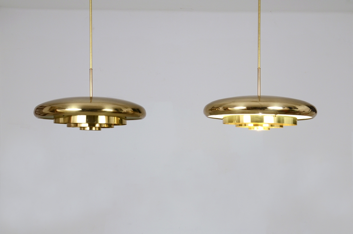 Rare pair of Bergboms pendant lamps, in polished brass, featuring shallow circular shades with geometric details underneath, suspended by slender vertical cords.