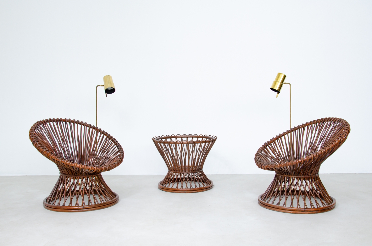 Pair of Bonacina rattan lounge chairs circa 1950, featuring woven oval-shaped reclining seats and conical bases, accompanied by a matching woven rattan side table with glass top, front view.