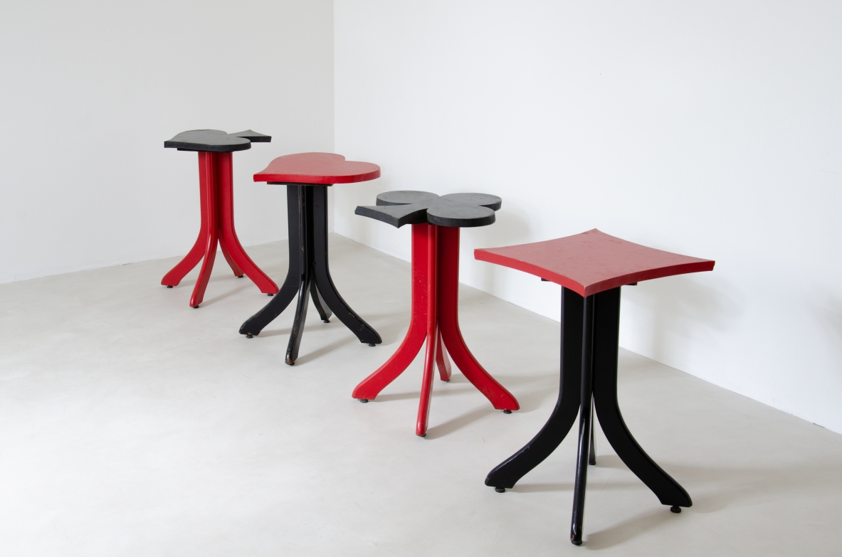 Group view of four 1930s Italian bar stools in red and black lacquered wood, with playing card suit-shaped seats representing hearts, spades, diamonds and clubs, and splayed legs.