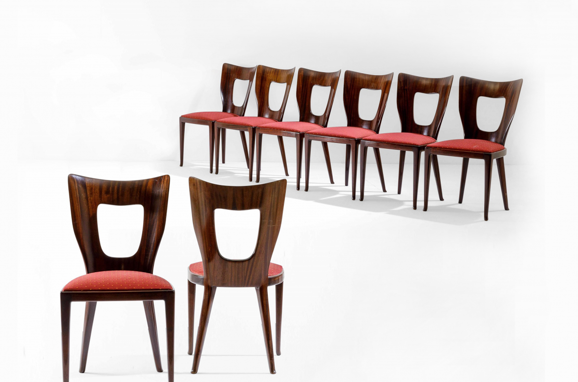 Group view of eight Osvaldo Borsani Triennale chairs in dark wood, with shaped open backrests and red upholstered seats, arranged on two levels.