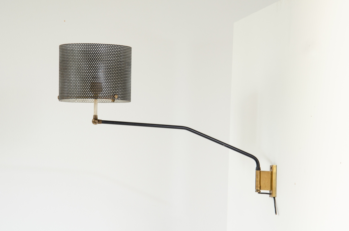 Stilnovo wall lamp featuring a long shaped tubular arm in dark metal, cylindrical metal mesh shade, brass details and wall mount, photographed from the side.