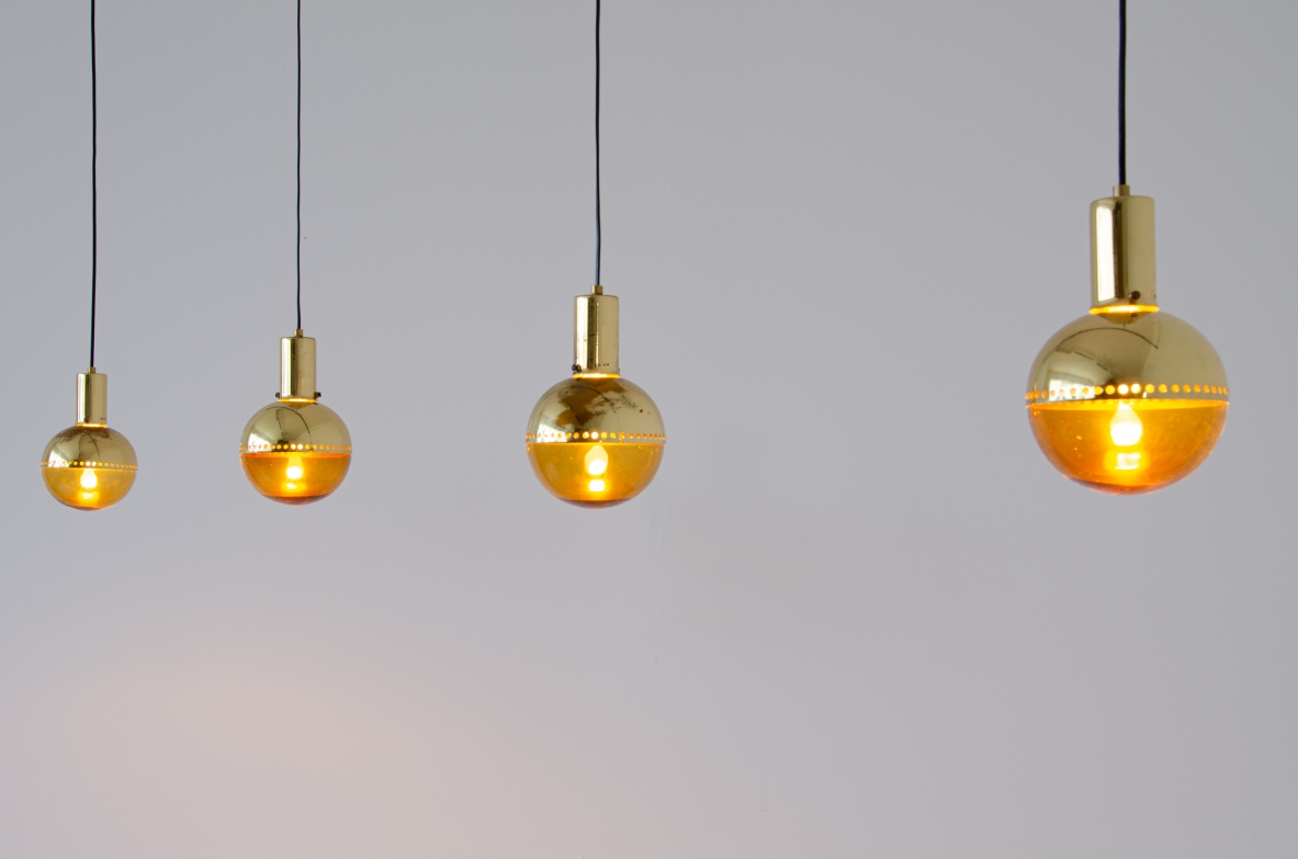 Set of four pendant lamps by Hans A. Jacobsson for HAJ Stockholm,featuring amber blown glass spherical shades in different sizes, cylindrical brass fittings and long suspension cords, front view.