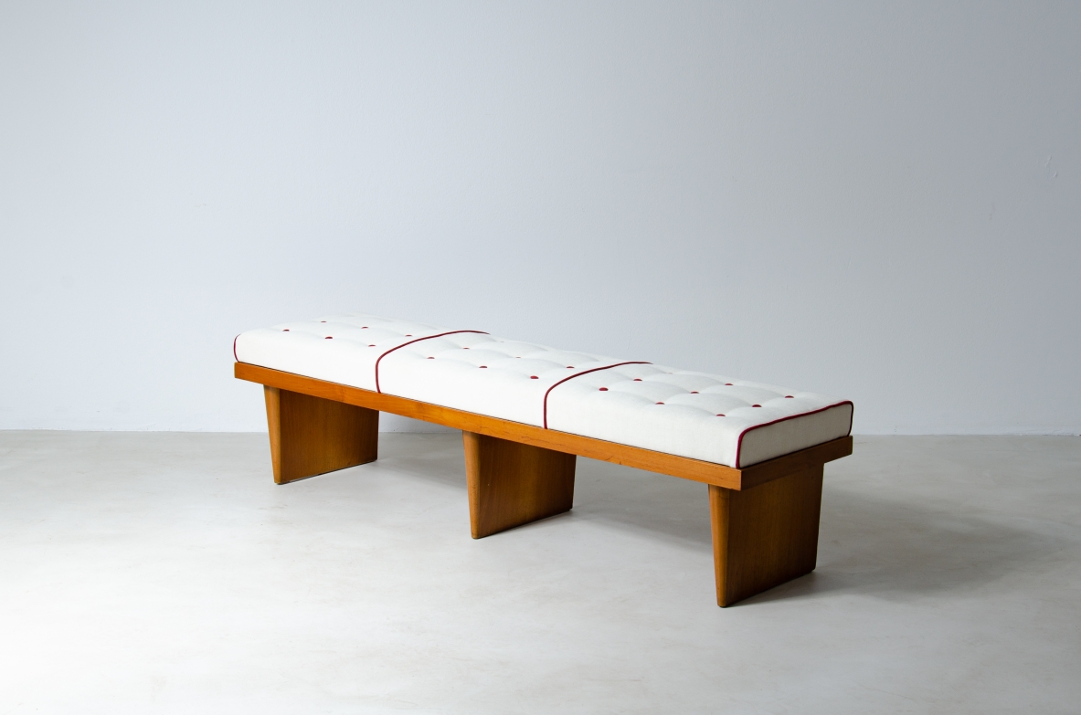 Front view of a long upholstered bench by Officina Antiquaria, featuring a wooden frame, three vertical supports and a white padded seat divided into three sections.
