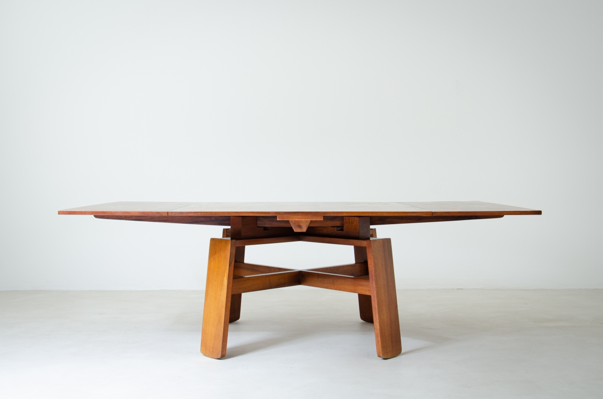 Silvio Coppola extendable walnut dining table for Bernini, 1964, with a broad wooden top and architectural cross-shaped pedestal base featuring angled supports and intersecting stretchers.