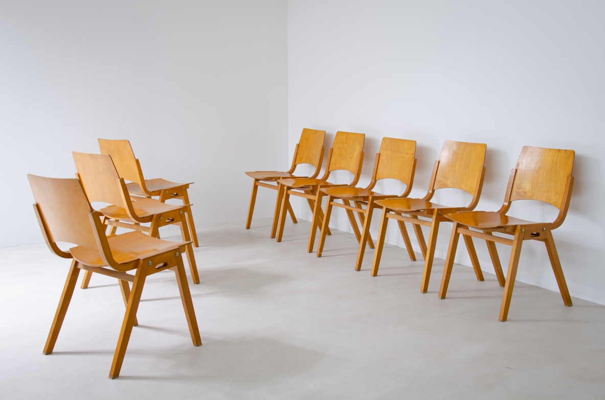Group view of eight Roland Rainer P7 chairs in light-colored curved plywood, with rectangular backrests, angled legs and some chairs with armrests.