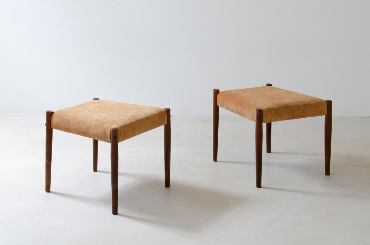 Angled view of two 1950s Italian stools with square beige upholstered seats and four slender dark wooden legs.
