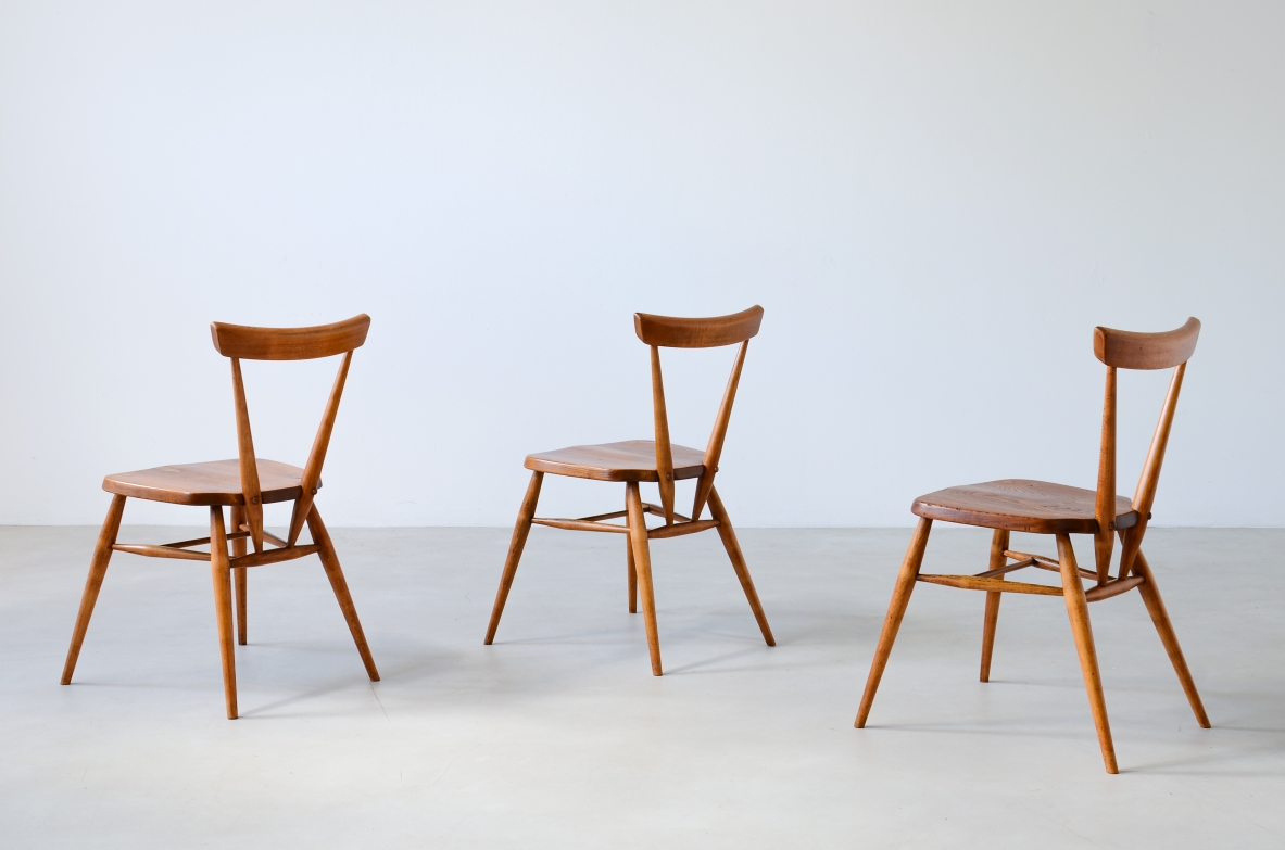 Group view of three Paul McCobb chairs in light oak, with curved open backrests, wooden seats and slender splayed legs.