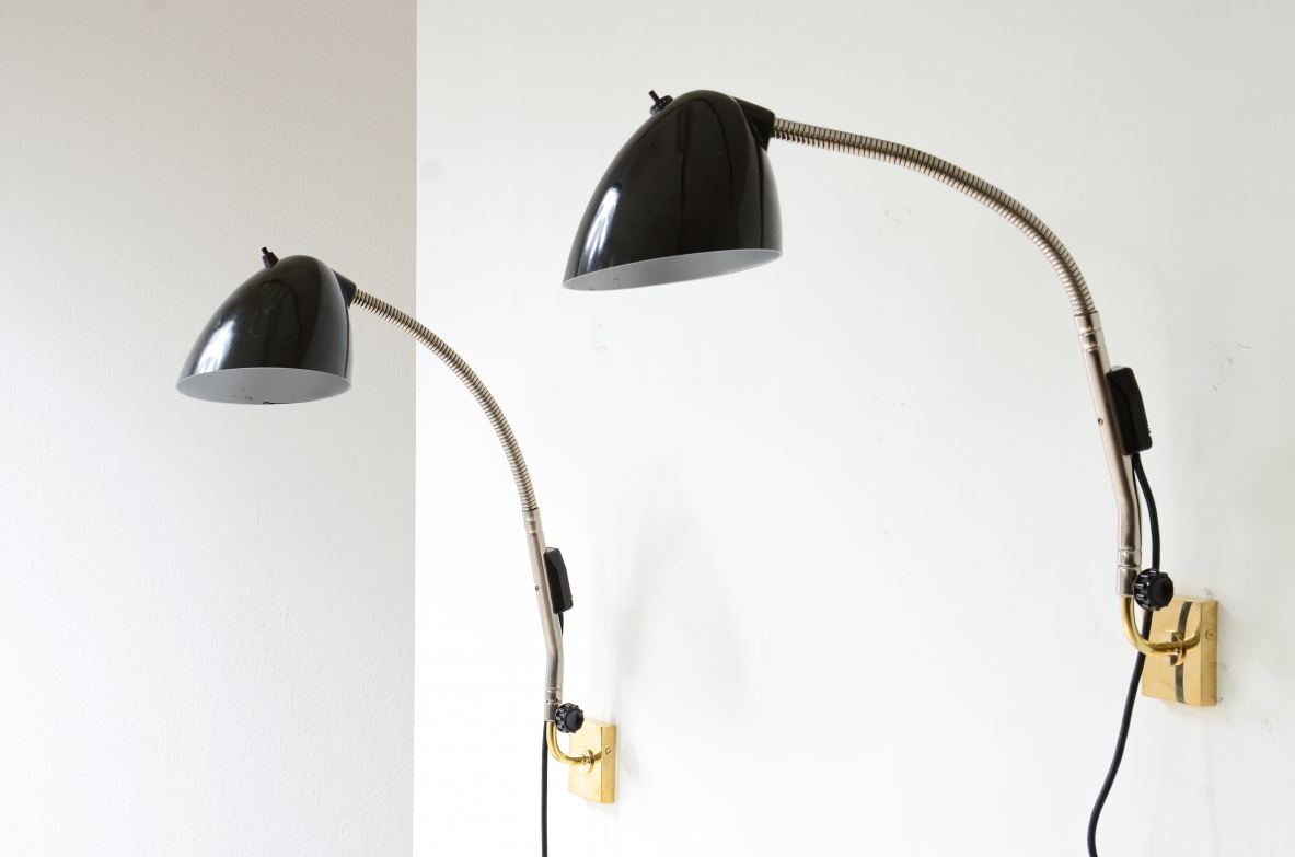 Pair of German wall lamps, featuring adjustable black Bakelite shades, long curved articulated metal arms and brass wall mounting plates, front view.
