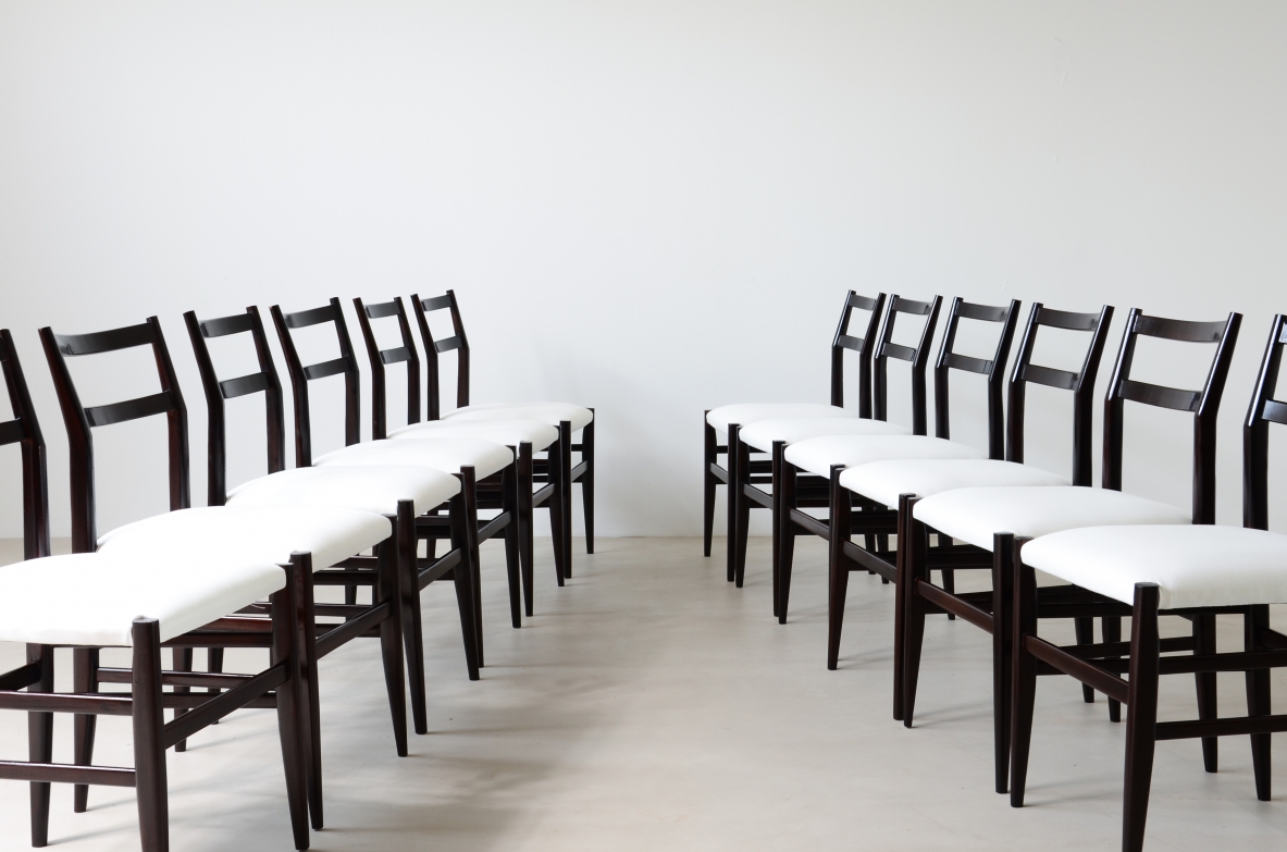 Group view of twelve Gio Ponti Leggera chairs by Cassina arranged in two facing rows, with dark wooden frames, open backrests and light-colored upholstered seats.