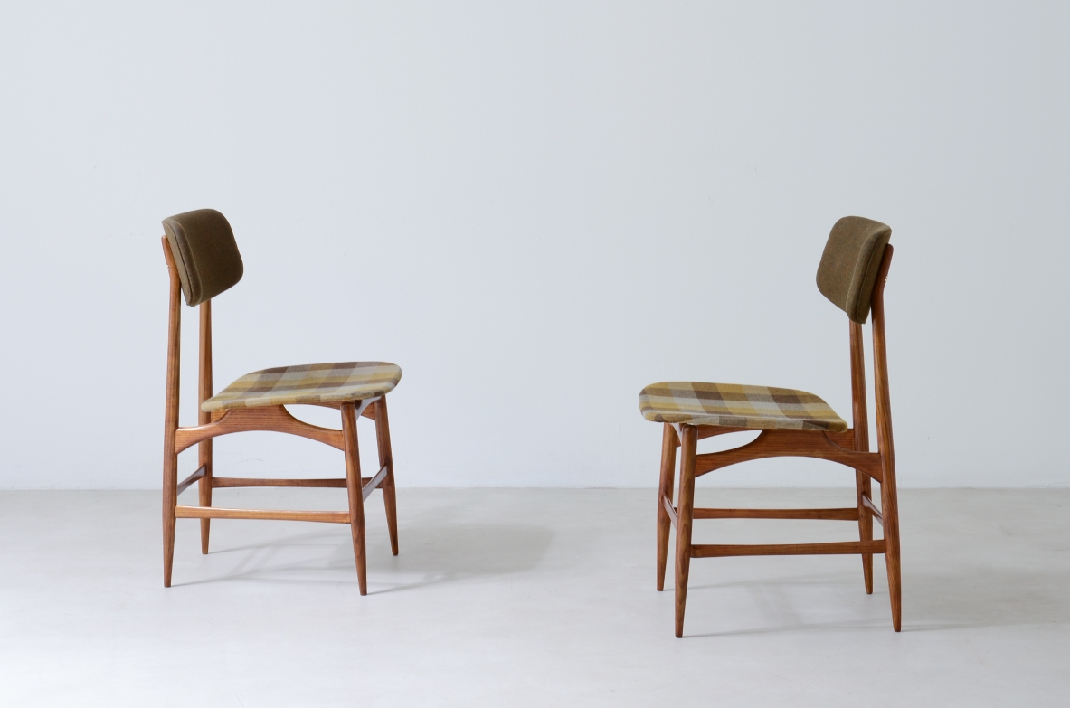Side view of two 1960s Italian chairs facing each other, with light wooden frames, upholstered seats and small padded backrests.