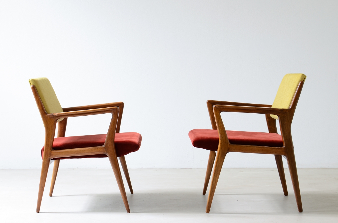 Side view of two modernist armchairs in the style of Gio Ponti, with shaped wooden frames, angular armrests, red upholstered seats and yellow backrests.