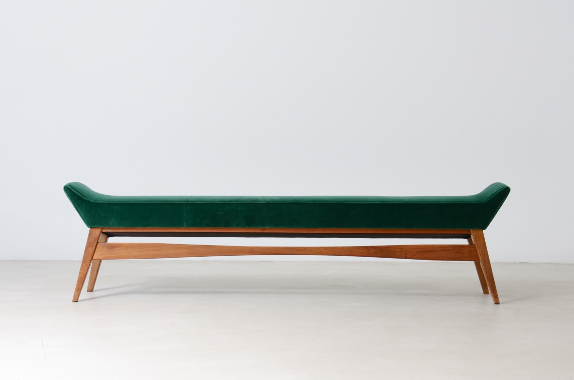 Side view of a long 1950s Italian bench with dark green upholstered seat, raised ends and a light wooden frame with angled legs.
