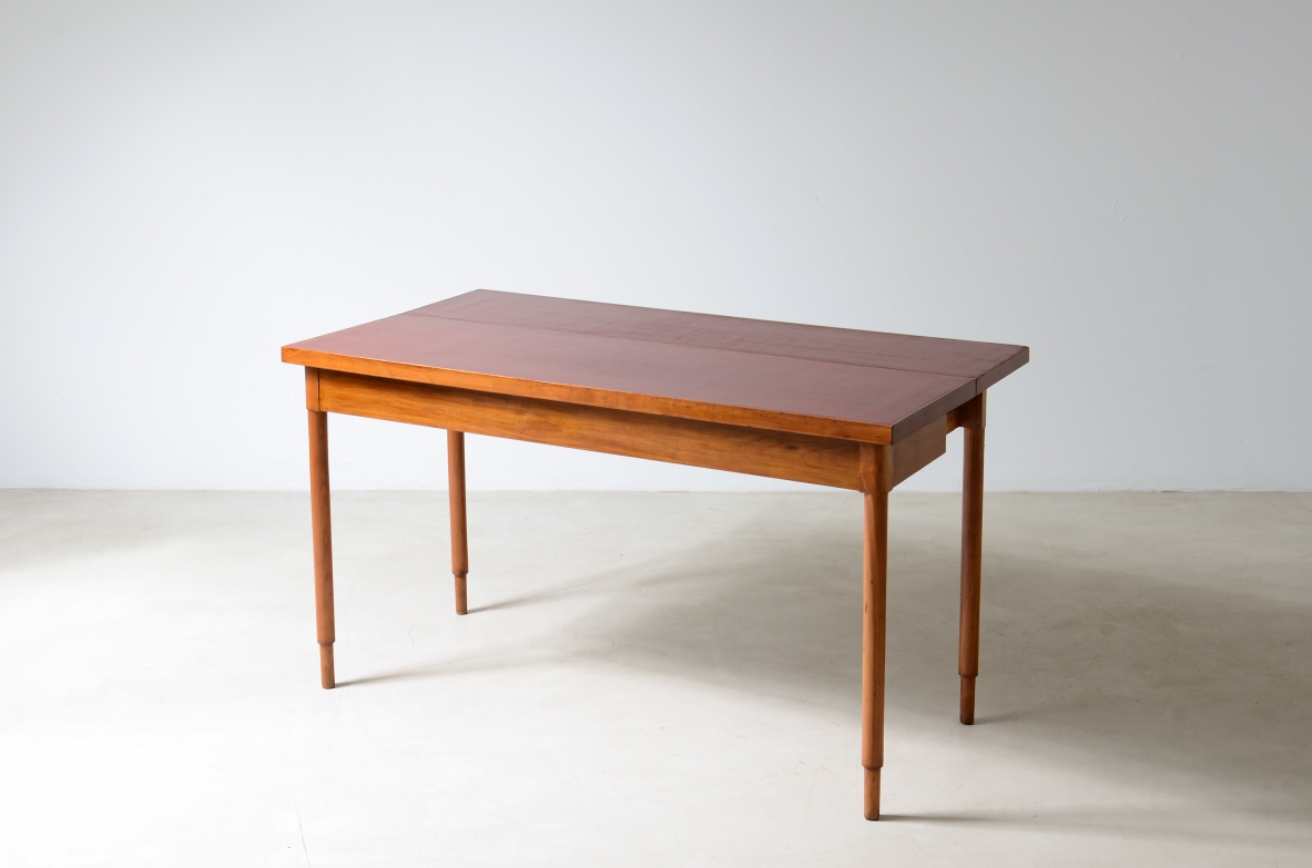 Italian walnut console table circa 1960 with rectangular red lacquered top and four slender tapered legs, photographed in three-quarter view.