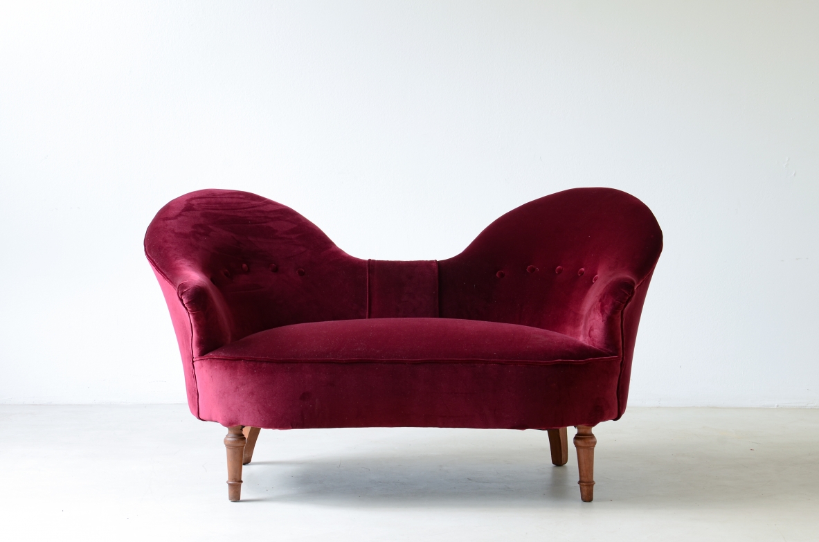 Cesare Lacca two-seater settee upholstered in cardinal red velvet, with a sculptural double-curved backrest, enveloping armrests and short turned wooden legs.