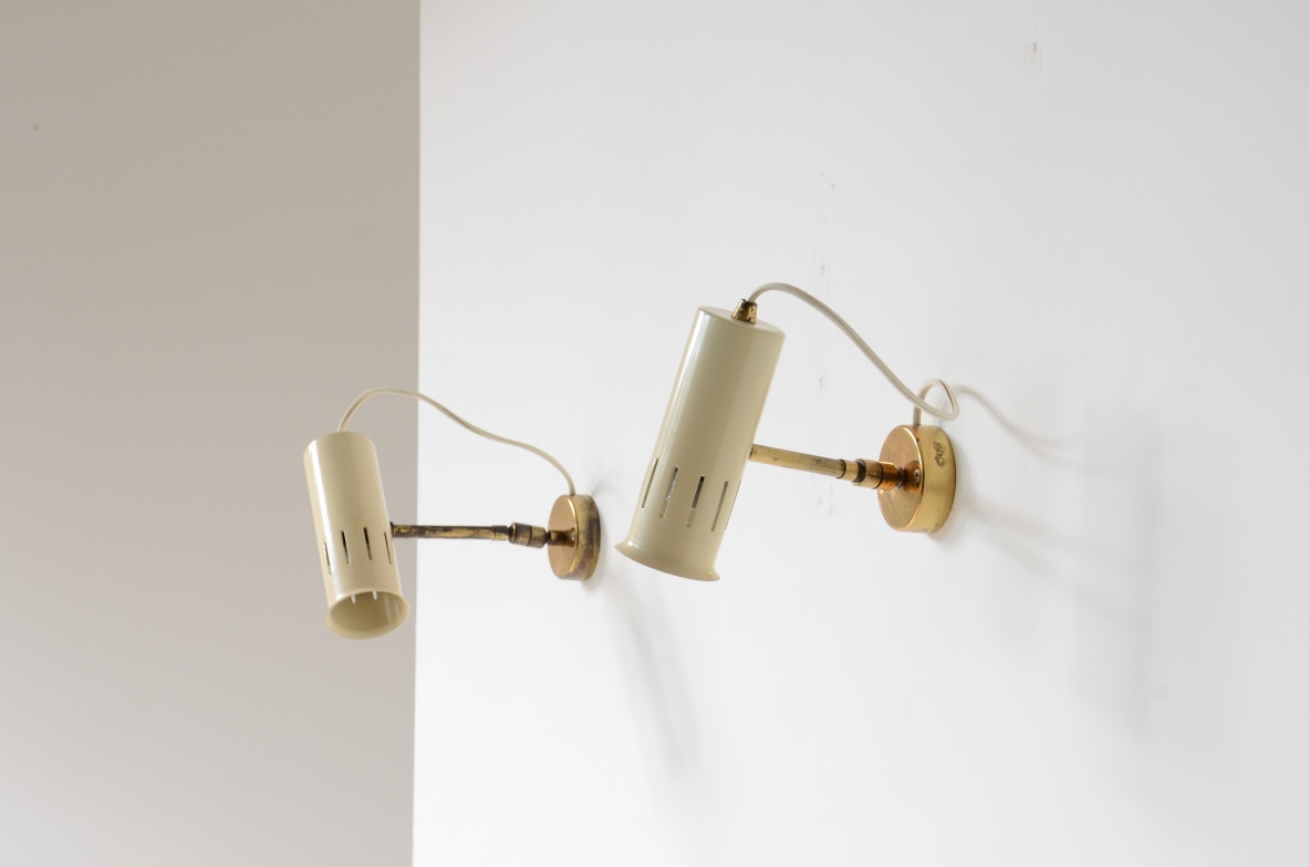 Pair of Italian adjustable wall lamps, featuring ivory lacquered cylindrical metal shades with vertical ventilation slots, brass arms and circular wall mounts.