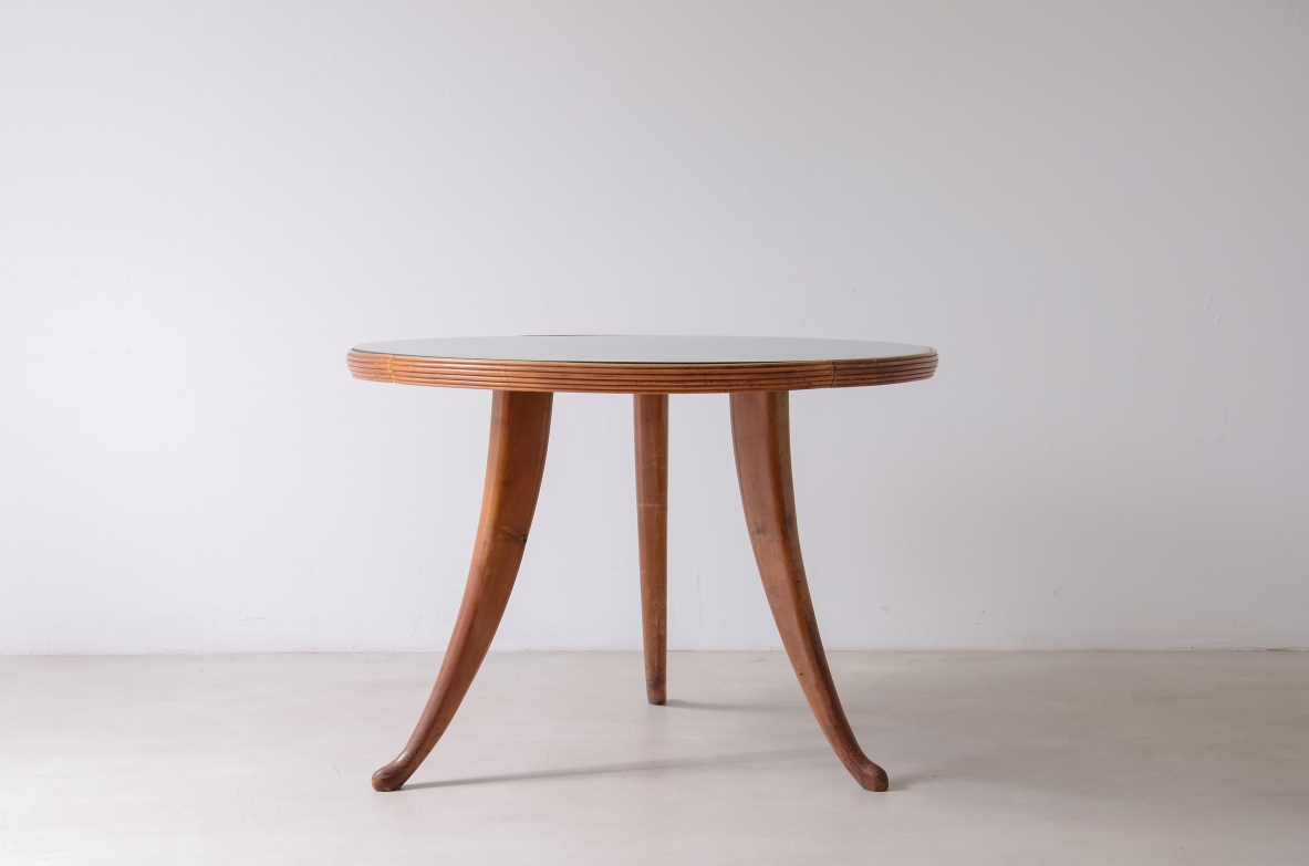 Italian 1940s round walnut table with three elegantly curved sabre legs, a reeded apron and a circular bevelled glass top, photographed beside a blue upholstered chair.