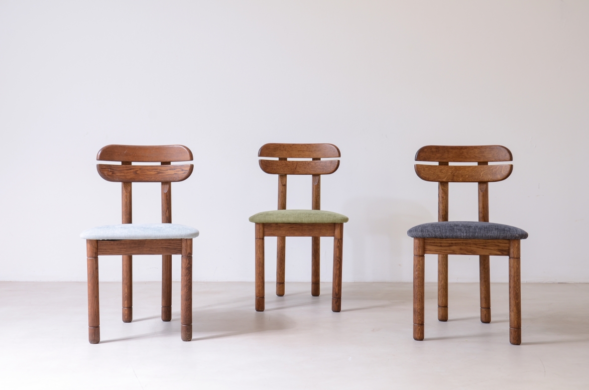 Front view of three 1960s oak chairs with shaped wooden backrests featuring two horizontal elements and upholstered seats in white, green and grey fabric.