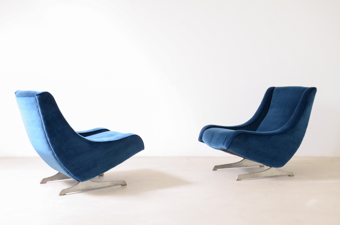 Side view of two Italian 1970s lounge chairs upholstered in blue velvet, featuring low seats, tall curved backrests and polished metal star-shaped bases.