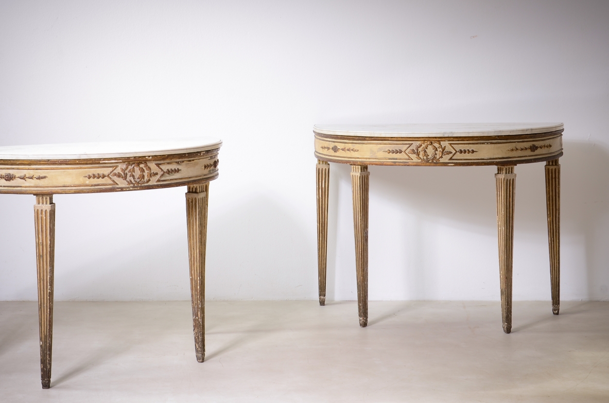 Pair of Italian Louis XVI demilune console tables, circa 1770, in lacquered and gilded wood with marble tops, finely carved aprons and tapered legs, front view.