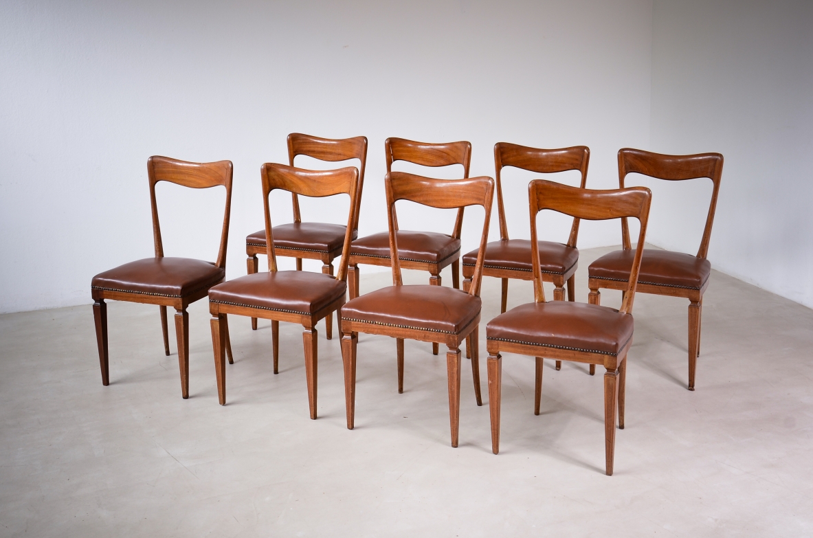 Group view of eight Gianni Vigorelli wooden chairs with shaped backrests and brown fabric-upholstered seats.