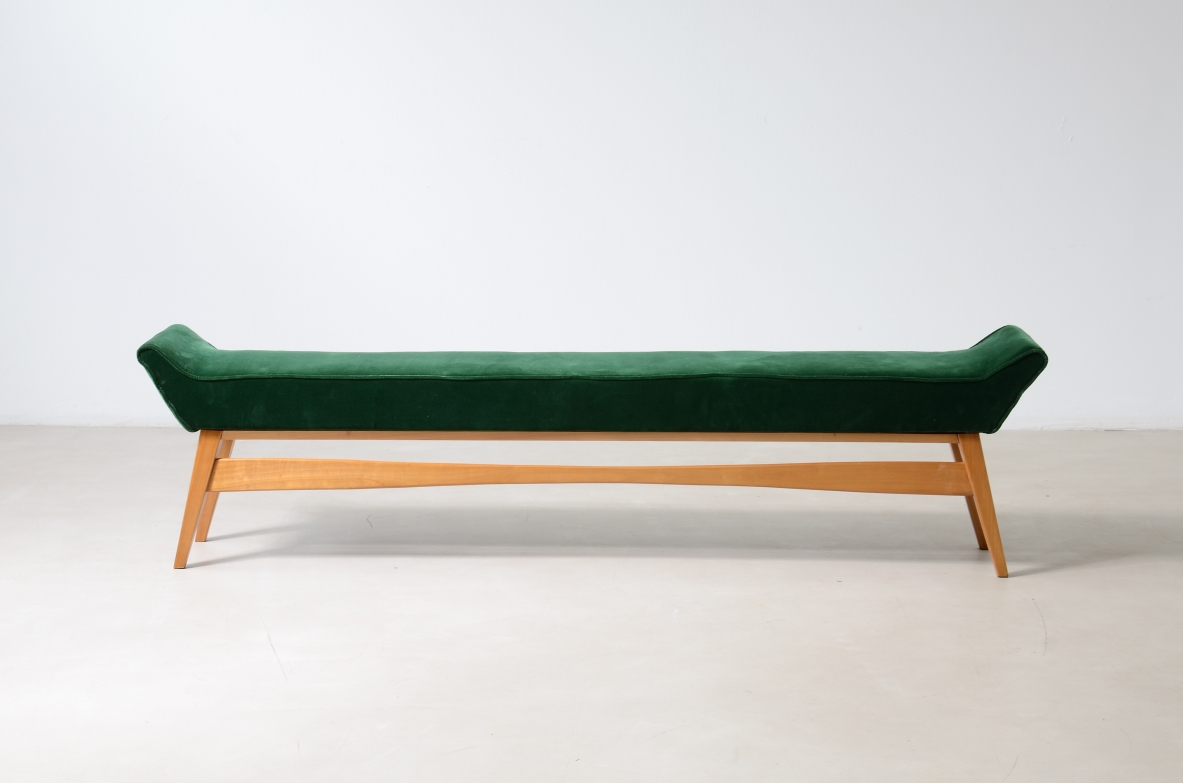 Side view of an Italian 1950s bench with a long dark green upholstered seat, raised curved ends, light wooden frame and angled legs.