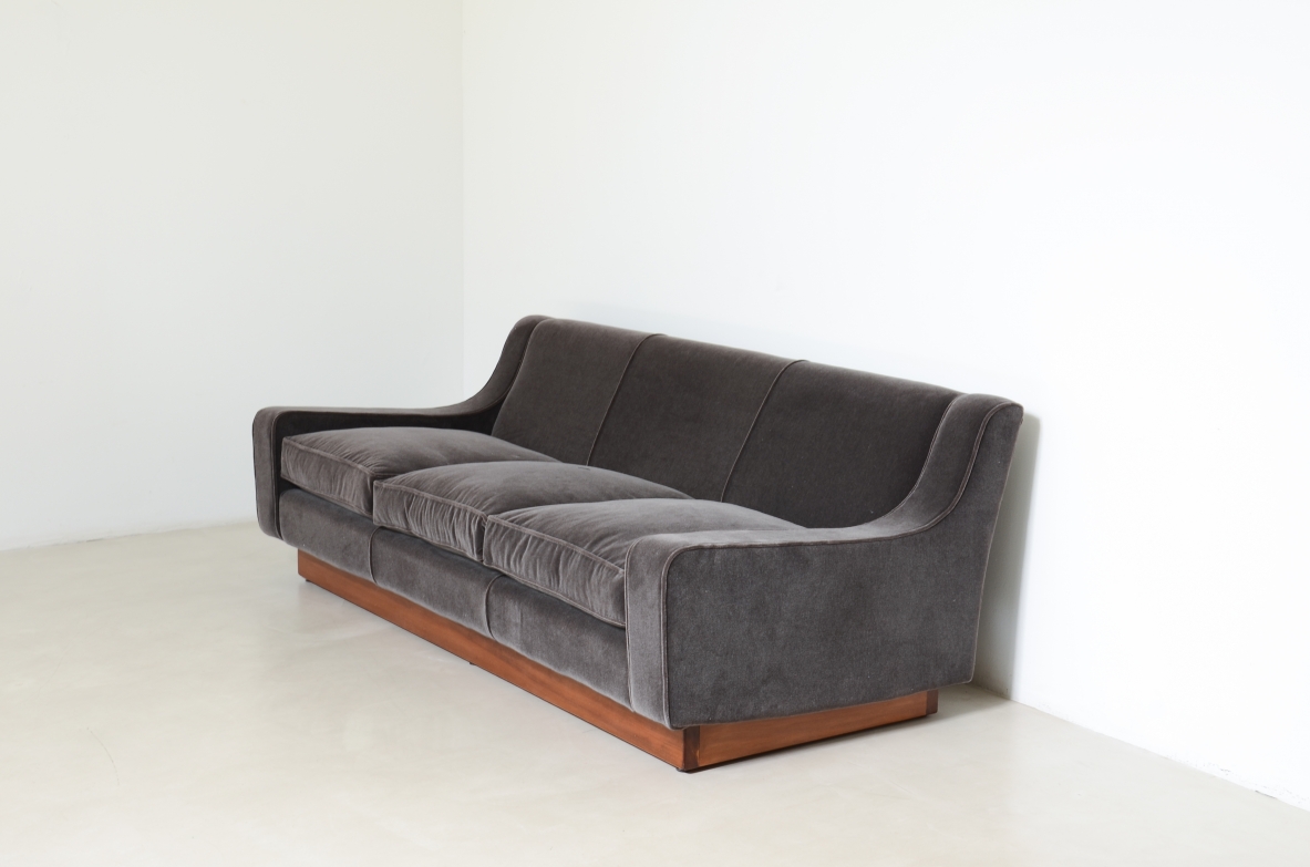 Three-seater sofa by Officina Antiquaria, upholstered in charcoal grey velvet, with a curved backrest, enveloping armrests and a wooden base.